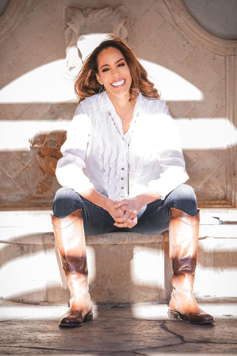A smiling woman in a white blouse and brown leather boots sitting on stone steps.