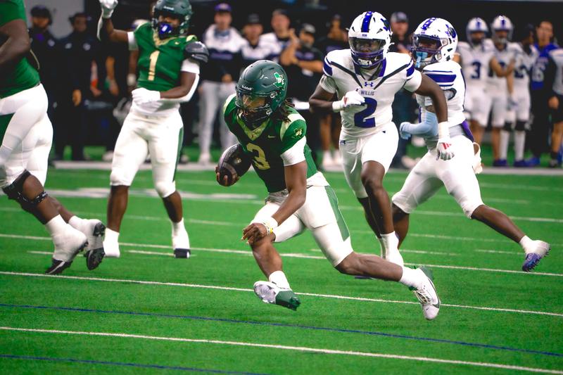 A football player in a green jersey carries the ball down the field while being chased by a defender.