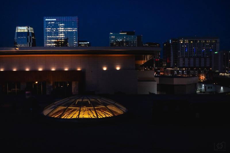 Modern architectural building with an illuminated glass dome at night against a downtown skyline.