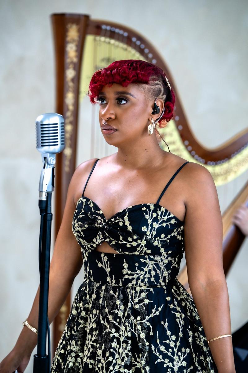 A musician with red hair wearing an in-ear monitor stands in front of a harp.
