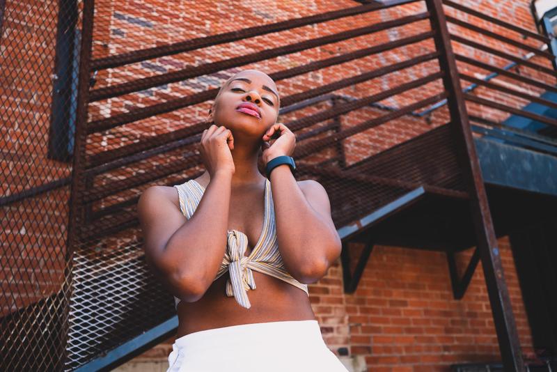 Low angle shot of a woman with short blonde hair posing outdoors in front of a brick building and metal fire escape.
