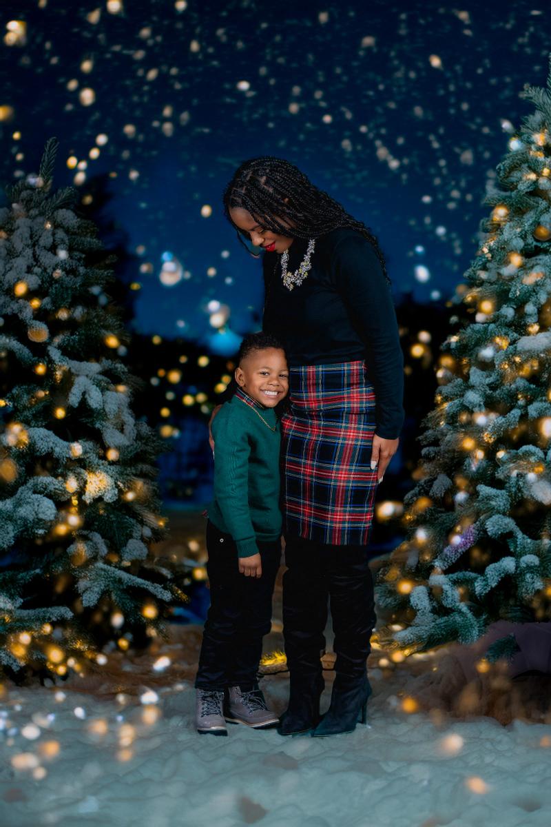 A woman and a young boy pose together in festive holiday clothing against a starry winter backdrop.