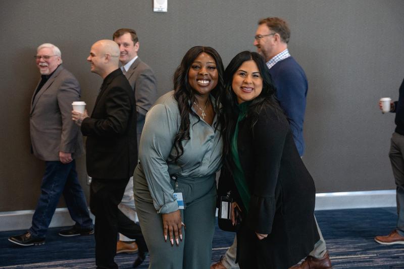 Two smiling women posing together at a corporate event while wearing name badges.