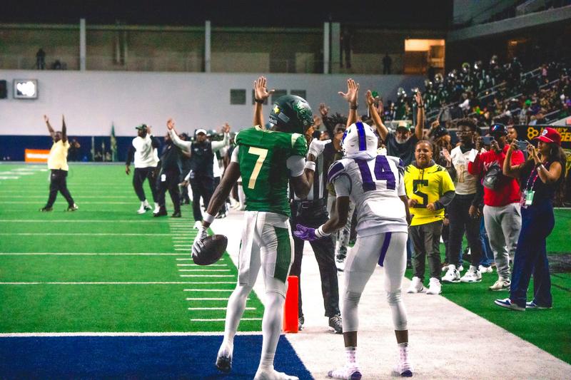 A football player in a green jersey number 7 celebrates in the end zone holding the football.