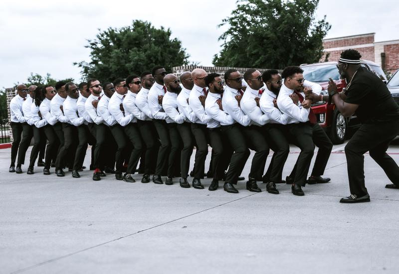 A line of men in matching white dress shirts, red ties, and sunglasses standing in formation outdoors.