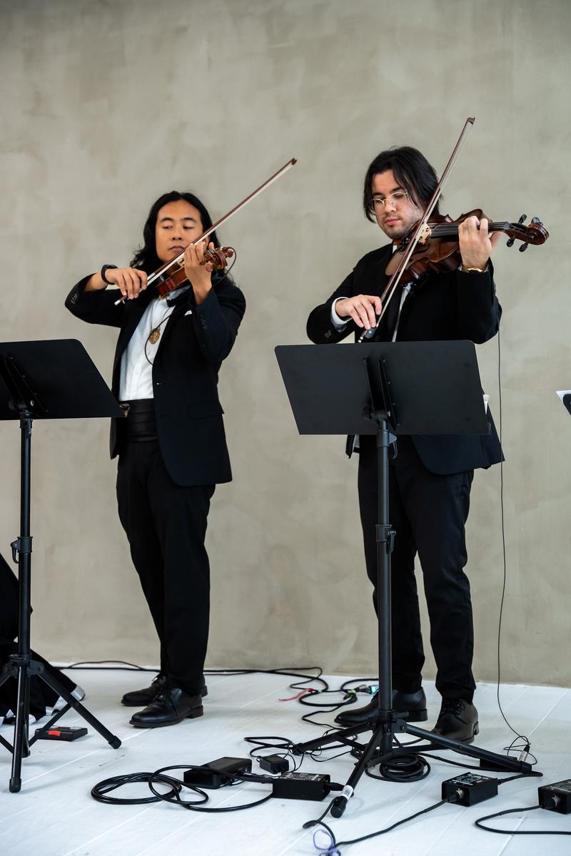 Two musicians in black suits performing on violin next to a music stand.