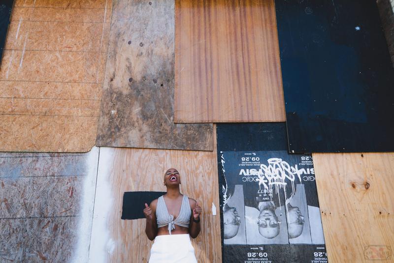 A woman laughing and looking up while posing in front of a wooden plywood wall with wheatpasted posters.