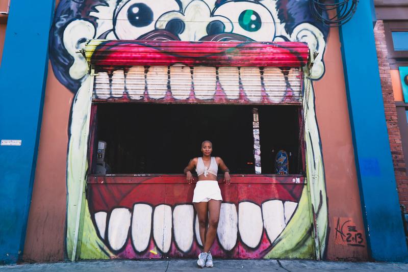 A woman poses in front of a vibrant graffiti mural on an urban building exterior.