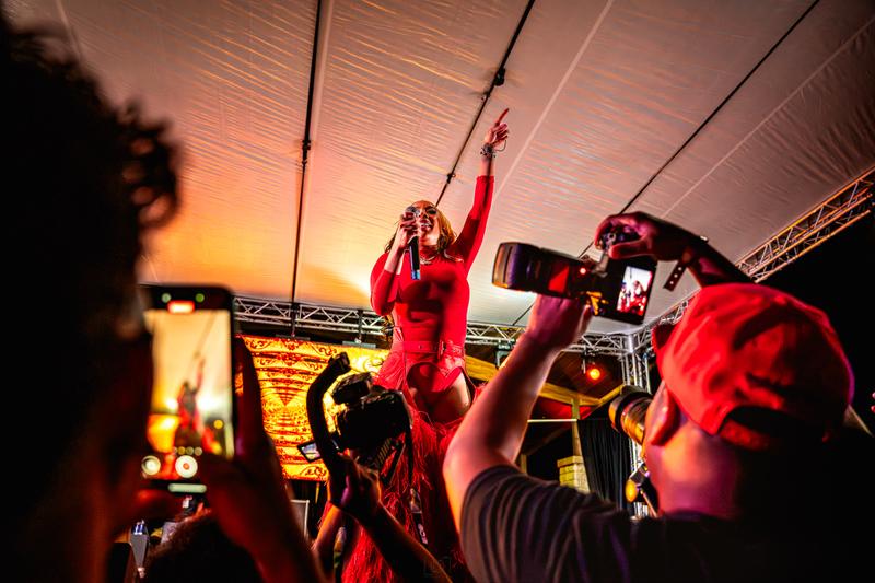 A female singer in a red outfit performs on stage with a microphone, pointing into the air.