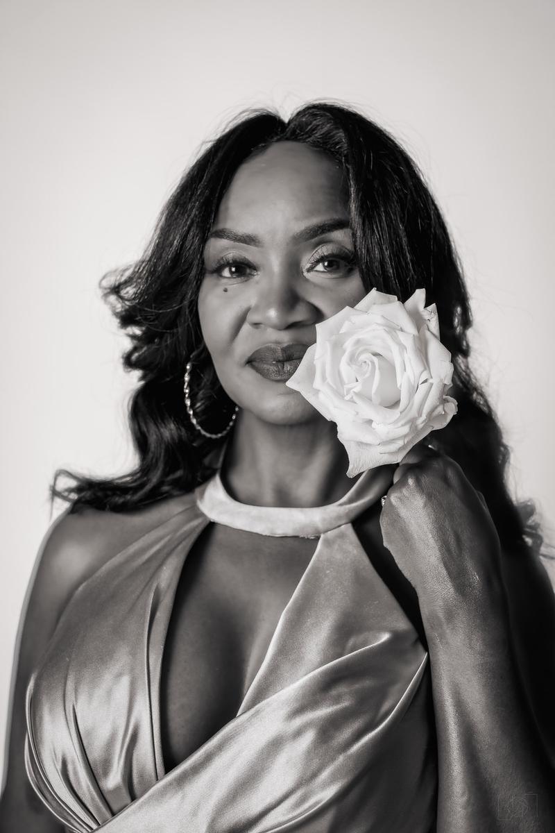 Black and white close-up portrait of a woman holding a white rose near her face.