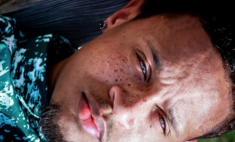 Extreme close-up portrait of a man with freckles looking at the camera while lying down.