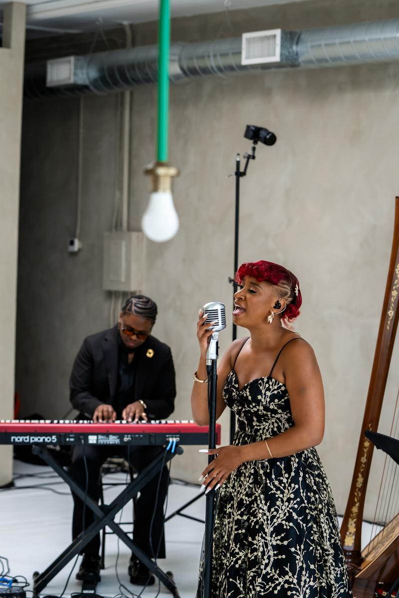 A woman with red hair sings into a vintage microphone accompanied by a keyboard player in the background.