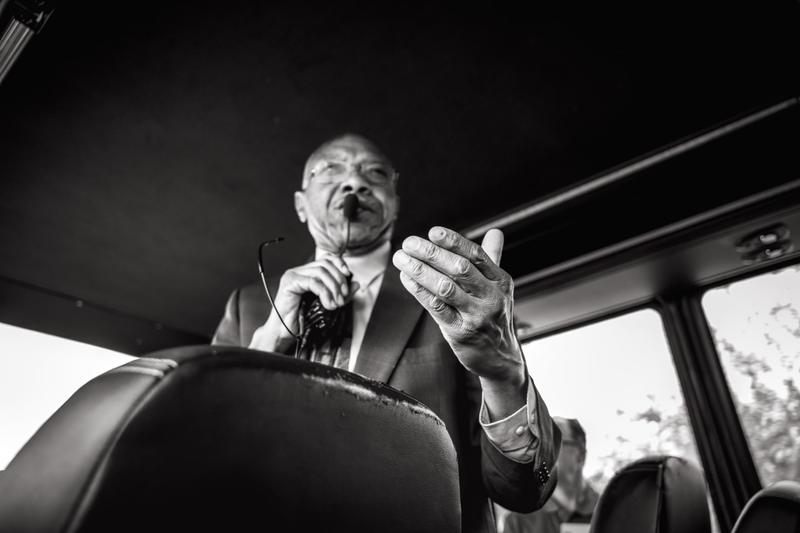 Black and white low-angle photo of a man in a suit gesturing while speaking into a microphone at a podium.