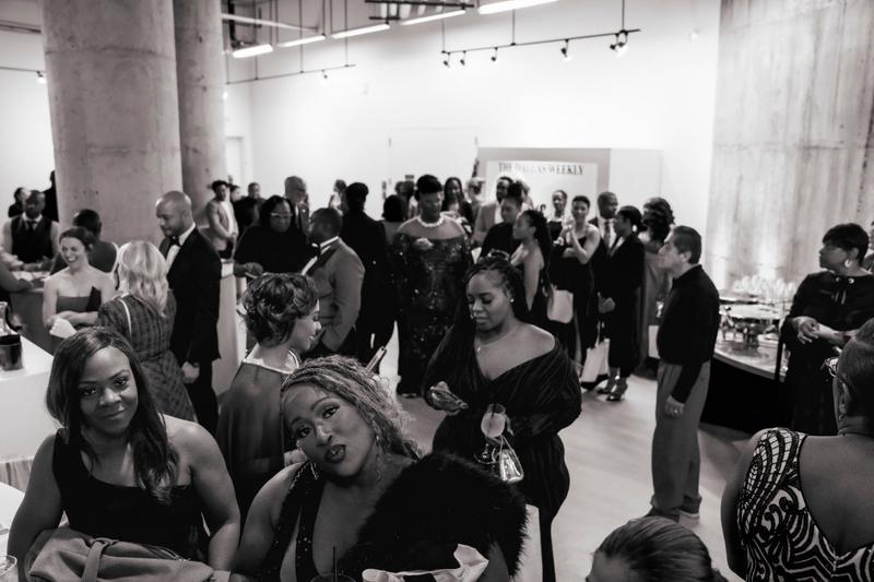 Black and white photo of guests in formal attire socializing at a gala event.