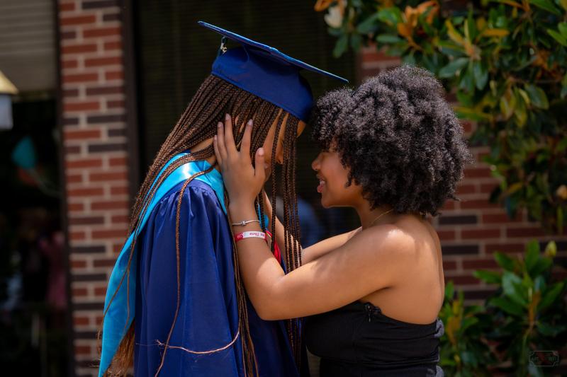Close-up of a woman smiling as she holds the face of a graduate wearing a blue cap and gown.