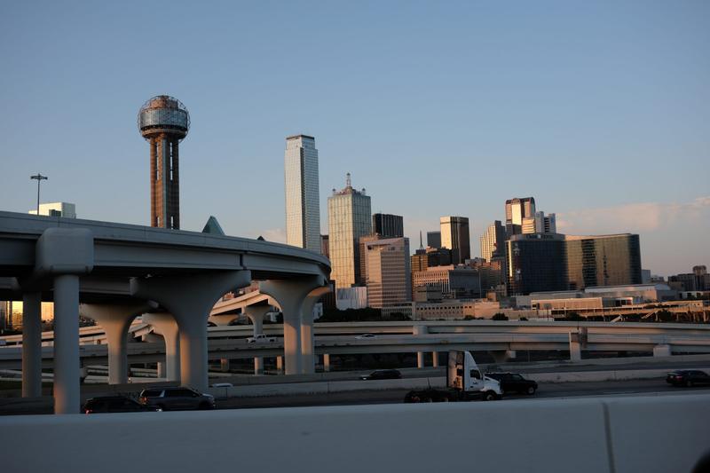 Downtown Dallas skyline featuring tall skyscrapers behind elevated highway overpasses in clear late afternoon light.