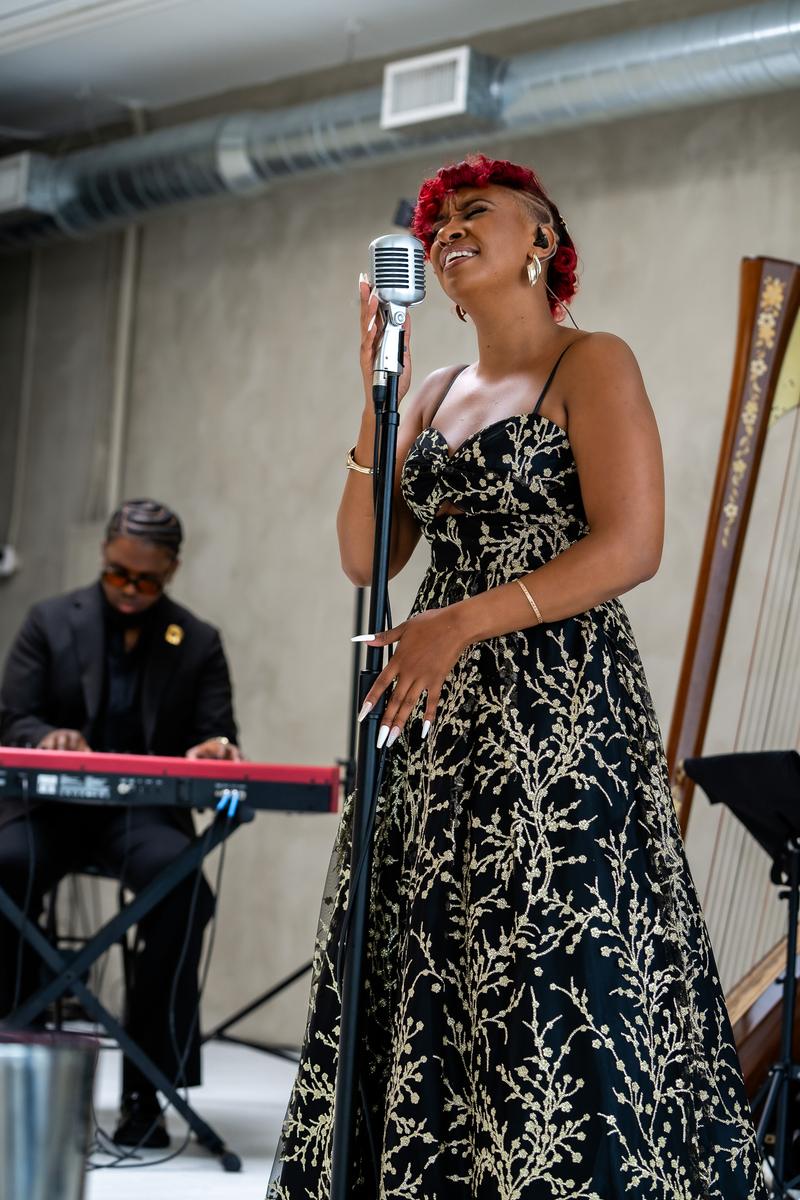 A singer with red hair in a black and gold patterned dress performs into a vintage microphone.