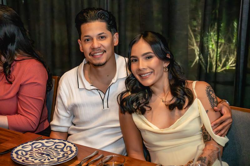 A smiling man and woman pose together closely at a dining table during an event.