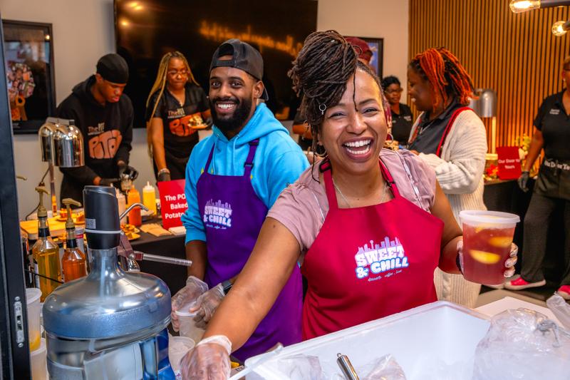 Two smiling business staff wearing branded Sweet and Chill aprons and food prep gloves behind a counter.