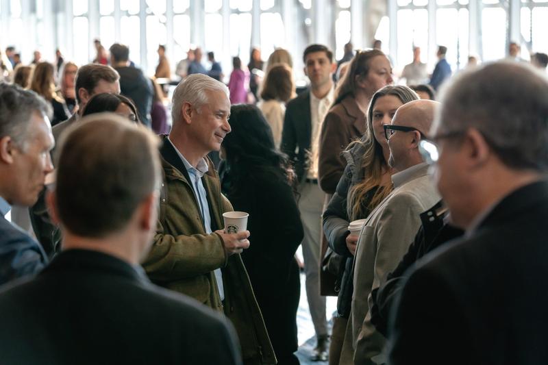 Attendees holding coffee cups and networking during a bright corporate event break.