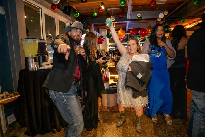 A woman raises a cocktail while guests celebrate at a festive holiday party.