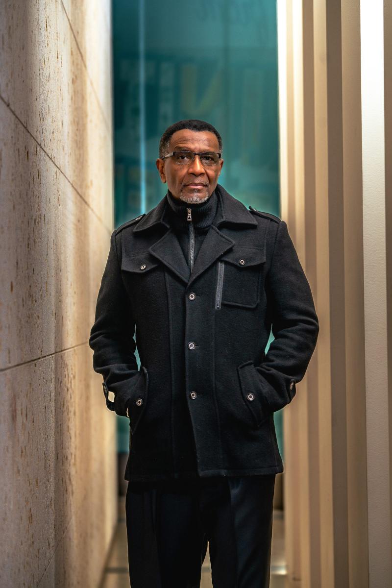 Portrait of a man wearing glasses and a black coat with hands in pockets.