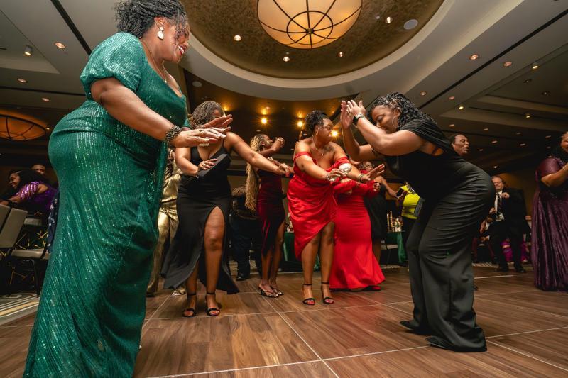 Guests dressed in formal gowns dancing on a wooden dance floor at an evening gala.