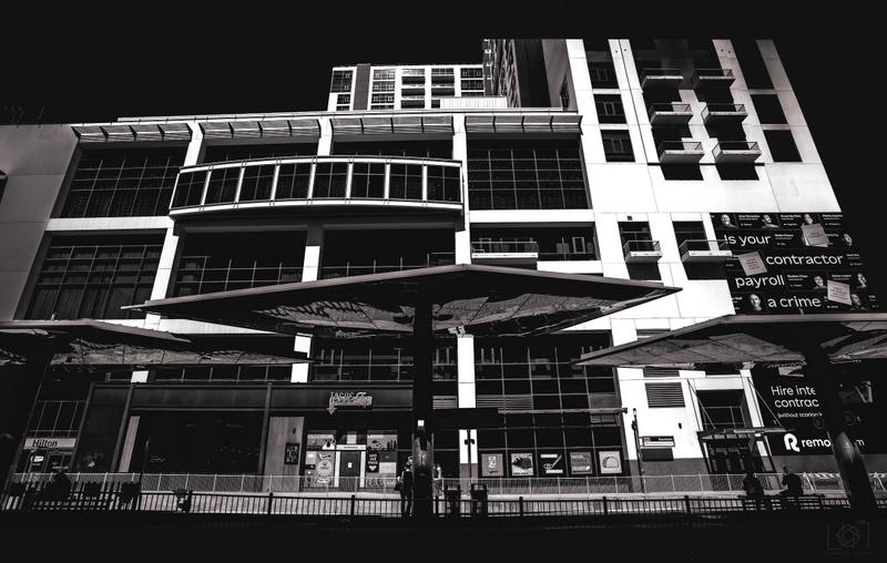 Black and white photograph looking up at a modern urban building exterior with storefront signs.