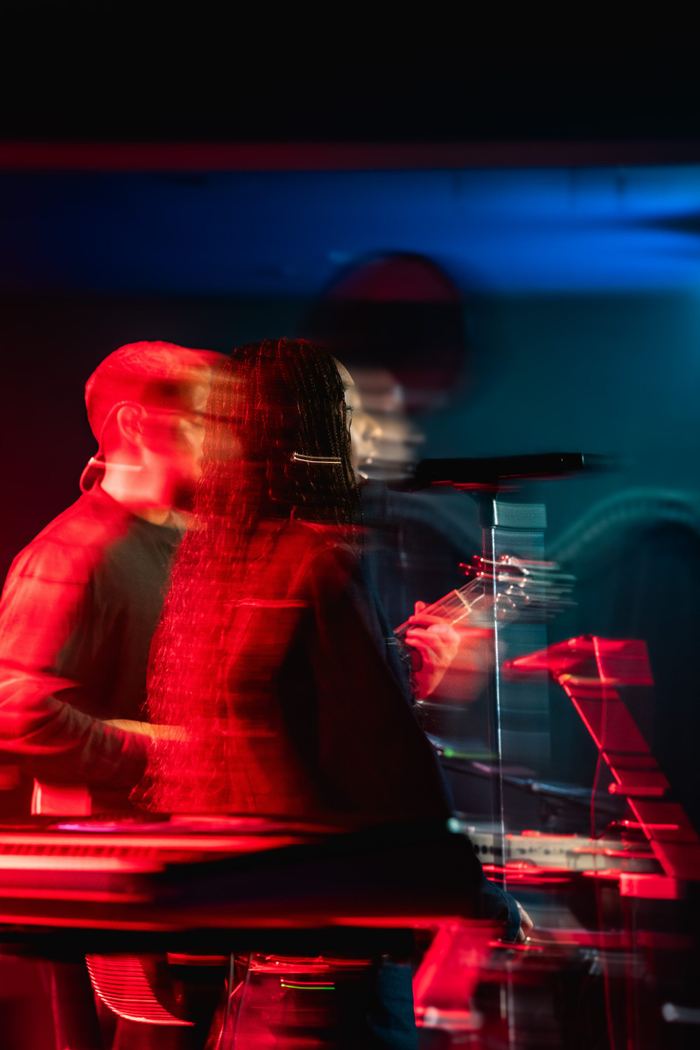 A musician with long braids performing under dramatic red and blue stage lights with motion blur.
