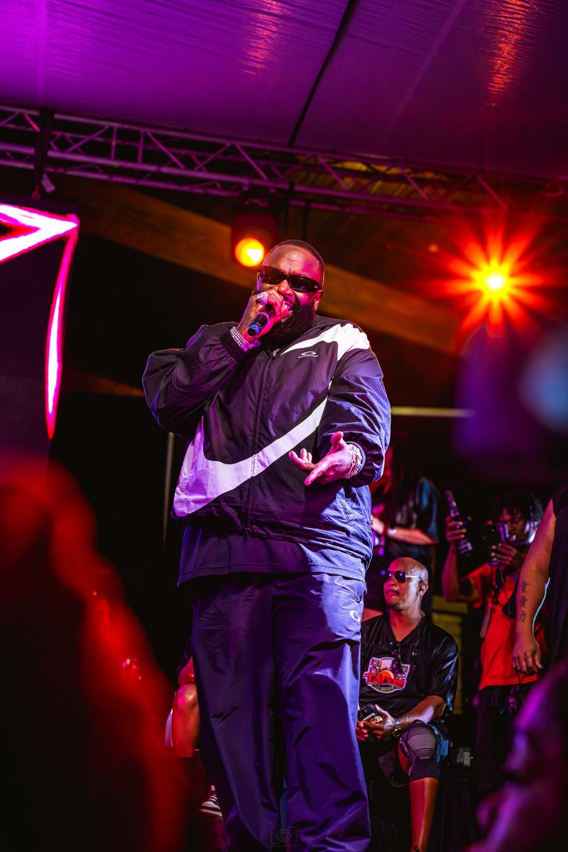 Musician performing live on stage into a microphone under purple and red stage lights.