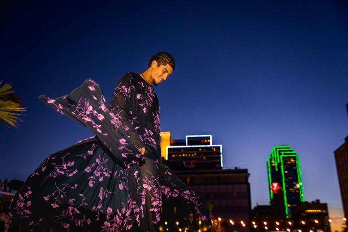 A model wearing a flowing black and purple floral outfit walks during an outdoor fashion show in Dallas at dusk.