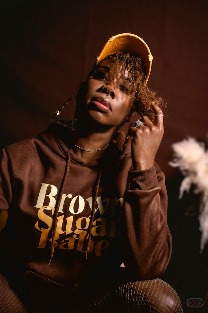 Close-up portrait of a woman wearing a yellow cap and a brown hoodie with gold lettering.