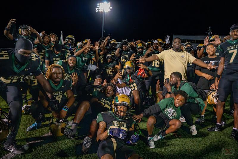 DeSoto High School football players celebrate on the field under stadium lights at night.