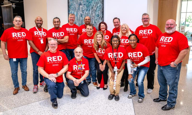 A group of corporate employees posing together in matching red RED Friday shirts.