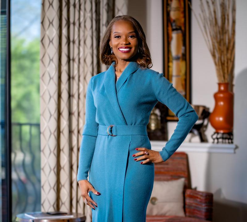 Portrait of a smiling woman posing in a teal belted dress.