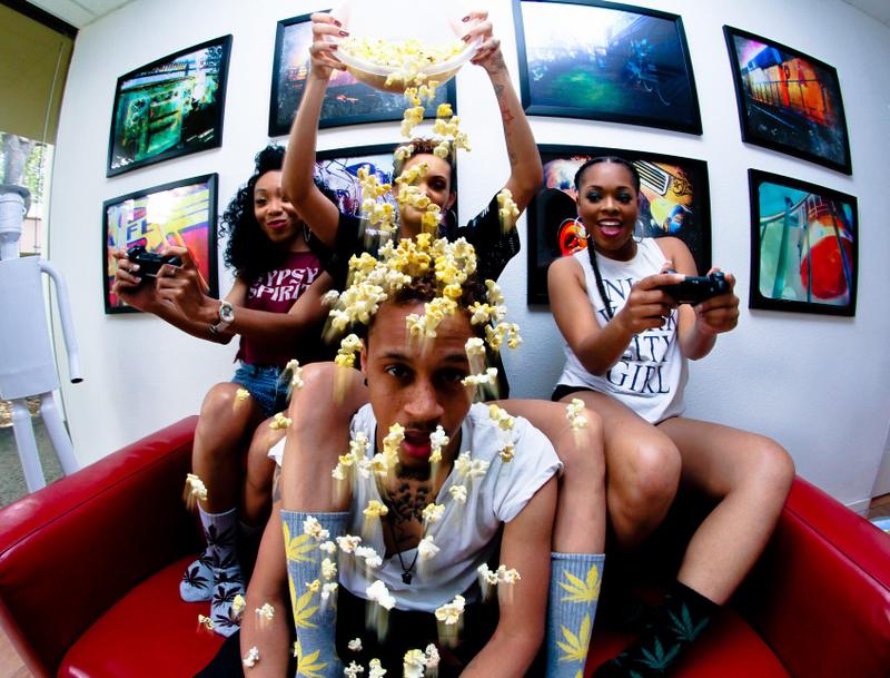 A group of friends laughing as a woman pours a bowl of popcorn over a man's head during a creative photo shoot.