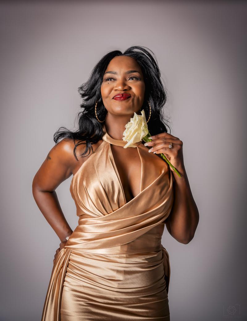 Portrait of a woman in a gold satin dress holding a white rose against a studio backdrop.