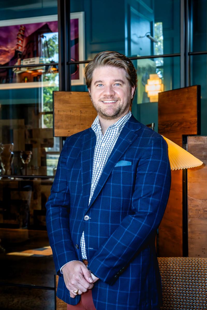 Smiling man in a blue windowpane suit jacket and patterned dress shirt posing for a portrait.