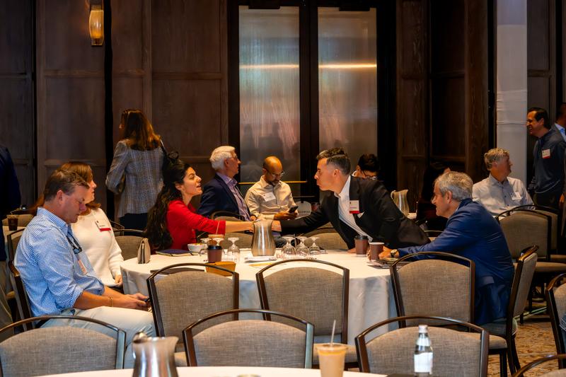 Attendees wearing name badges shake hands across a banquet table during a professional networking event.
