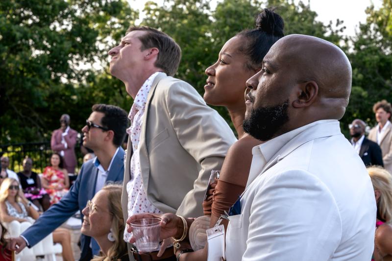 Side profile of attendees wearing event badges and holding drinks at an outdoor gathering.