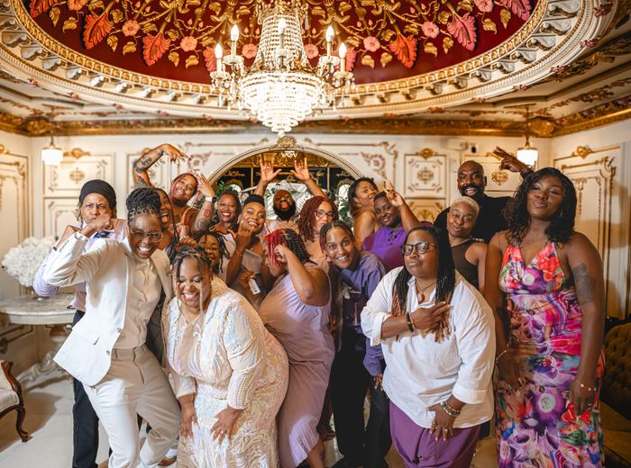 A group of cheerful guests posing together under an ornate crystal chandelier at a formal event.